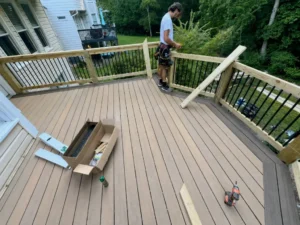 Worker installing gray composite deck boards inside natural wood railings