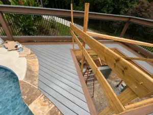 Angled gray composite pool deck under construction with natural wood railings