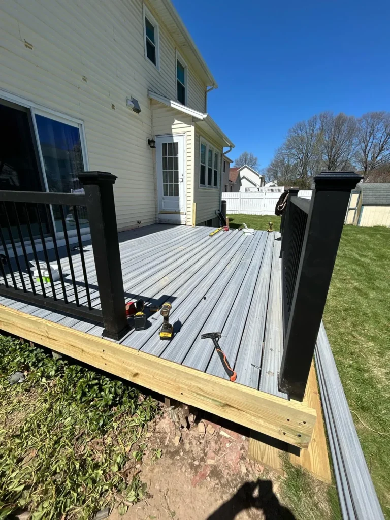 Low floating deck under construction beside a home with gray boards and dark railing posts