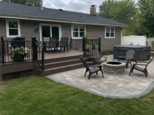 Paver patio with a stone fire pit, outdoor chairs, and a hot tub beside a raised backyard deck