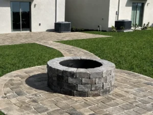 Curved paver patio with a round stone fire pit and walkway leading to the house
