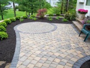 Backyard paver patio with a circular design, dark border, and landscaped garden beds