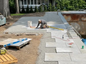 Contractor installing large patio pavers beside a swimming pool during construction
