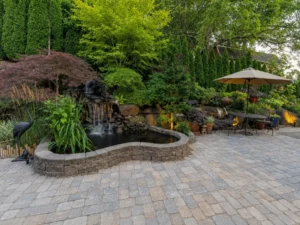 Landscaped paver patio with a waterfall pond and outdoor seating under an umbrella