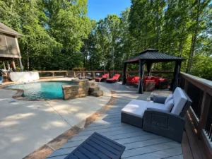 Gray poolside deck with wood railings, a black gazebo, and lounge seating