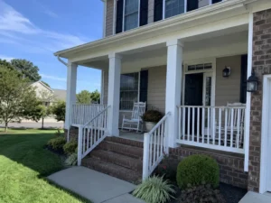 White farmhouse front porch with columns, gray steps, and white railings