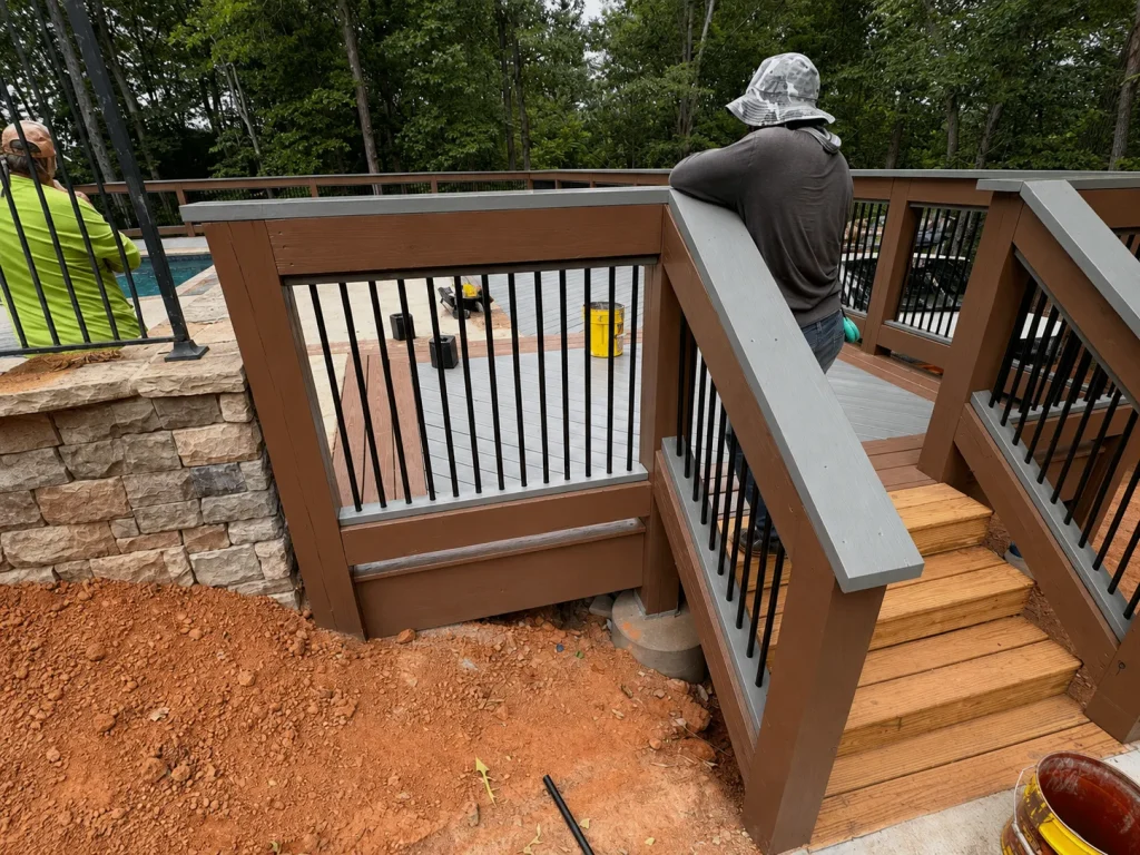 Contractor installing brown deck boards and black metal balusters on a raised deck