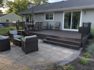 Brown backyard deck connected to a gray paver patio with lounge furniture