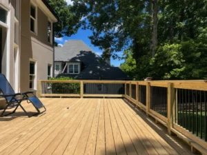 Large natural wood deck with black balusters and a shaded backyard view